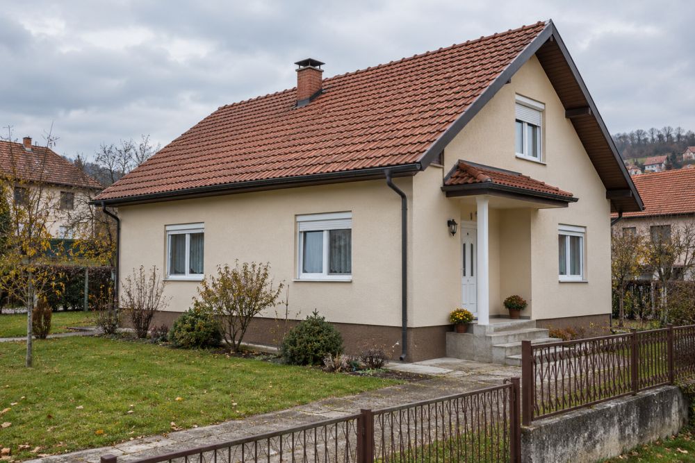 Prosečna porodična kuća sa fasadom, PVC stolarijom, kosim krovom i uređenim dvorištem.